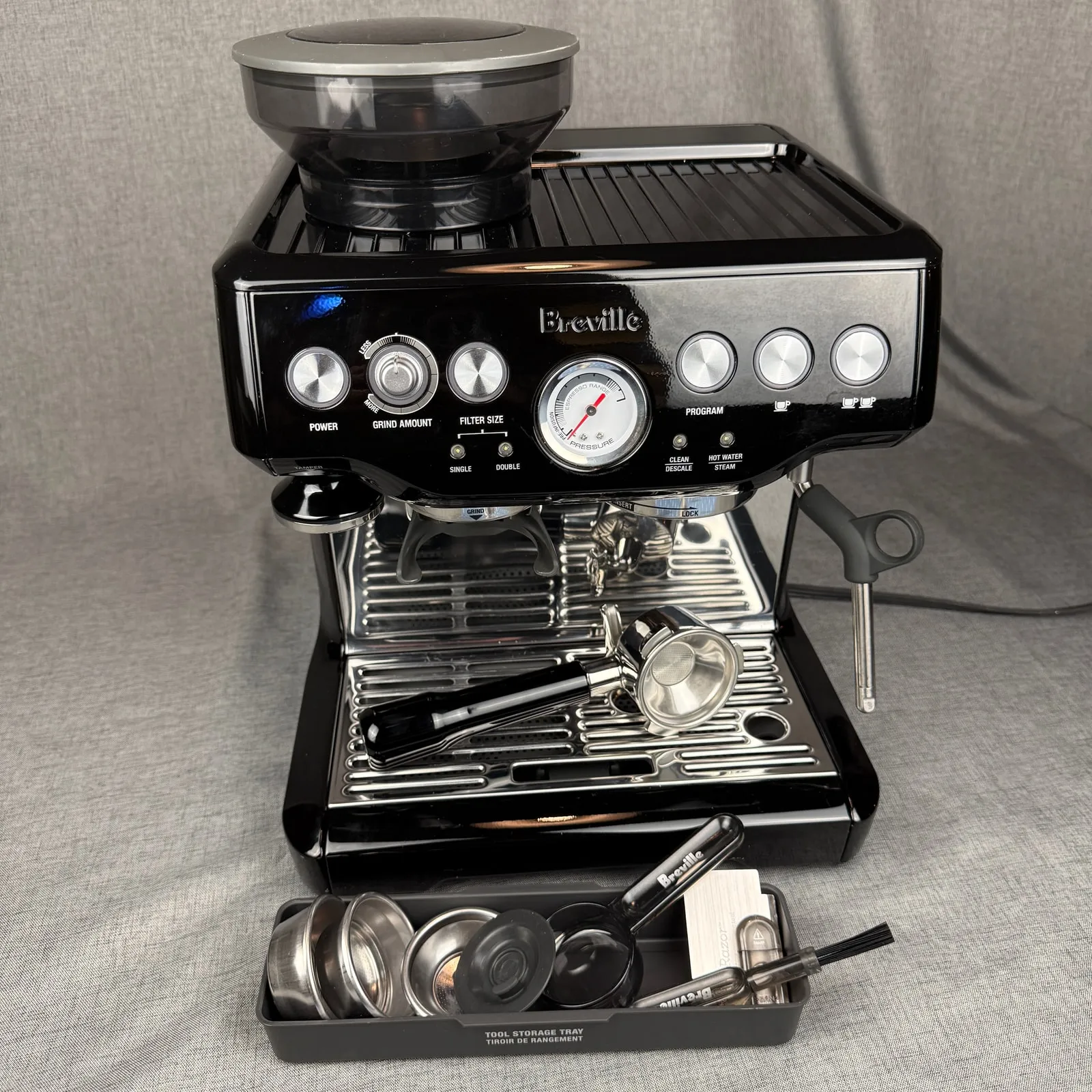 Breville Barista Express espresso machine in black, with its portafilter on the drip tray and a tool tray of filter baskets in front